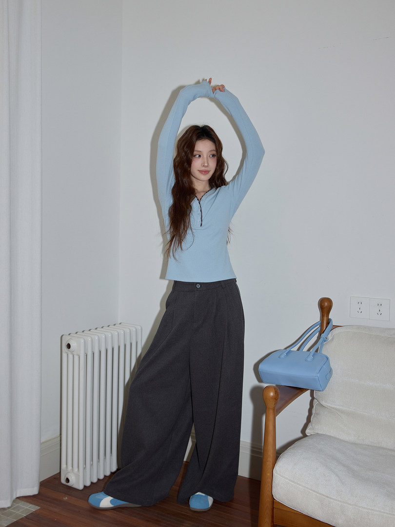Model wearing a light blue long-sleeve top with dark wide-leg pants and a blue handbag