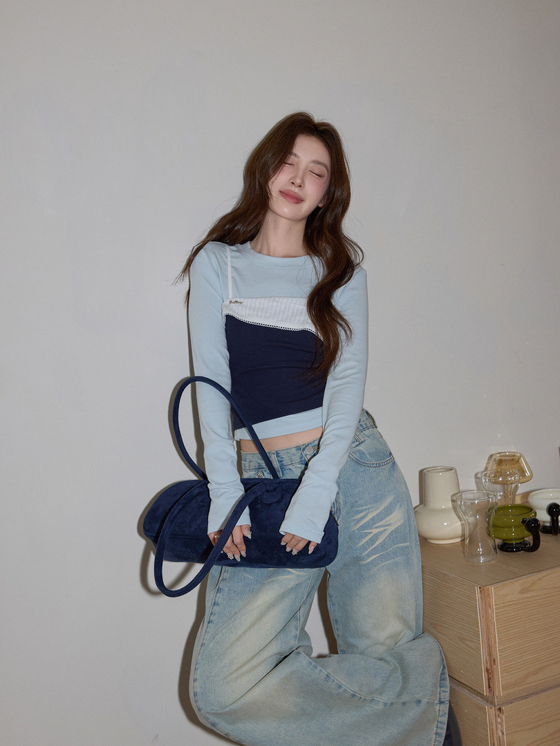 Model wearing a light blue long-sleeve top with wide-leg jeans and a navy shoulder bag