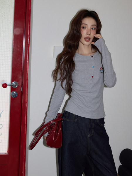 Model wearing a gray long-sleeve top with dark jeans and holding a glossy red handbag