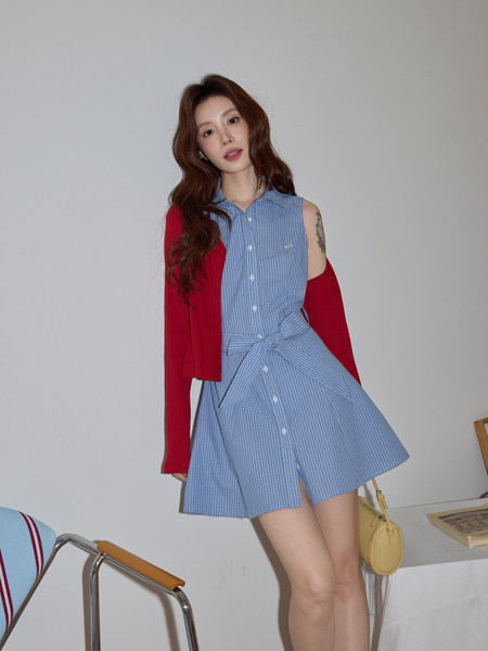 Model wearing a blue checkered sleeveless shirt dress with a red cardigan draped over her shoulders