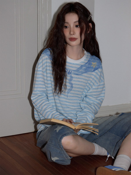 Model wearing a light blue striped long-sleeve top with denim shorts while sitting indoors