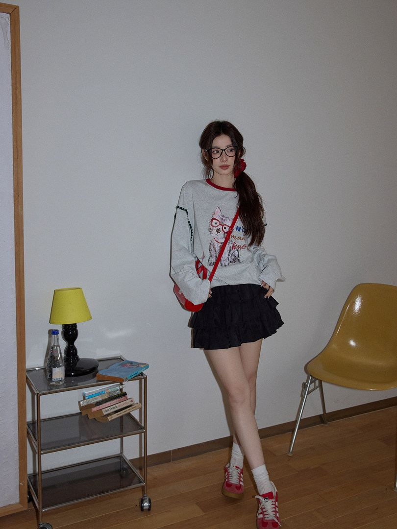 Woman wearing a graphic oversized sweatshirt, black pleated skirt, and red sneakers