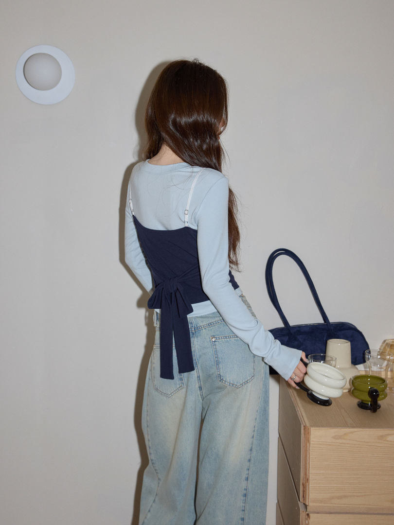 Model wearing a light blue long-sleeve top with a navy back-tie corset layer and loose light-wash jeans