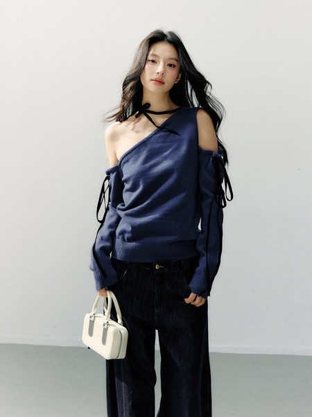 Model wearing a navy off-shoulder long-sleeve top with dark pants and a small white handbag