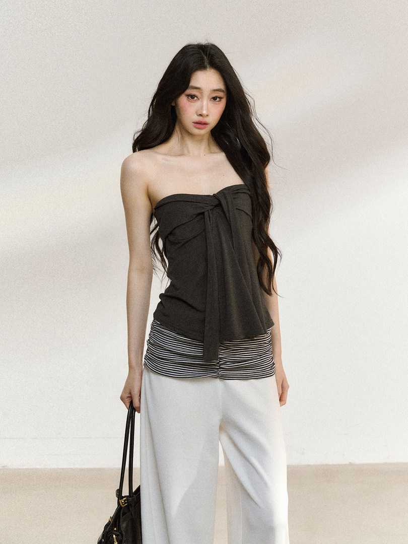 Model wearing a black strapless top with striped layered detail and white wide-leg pants