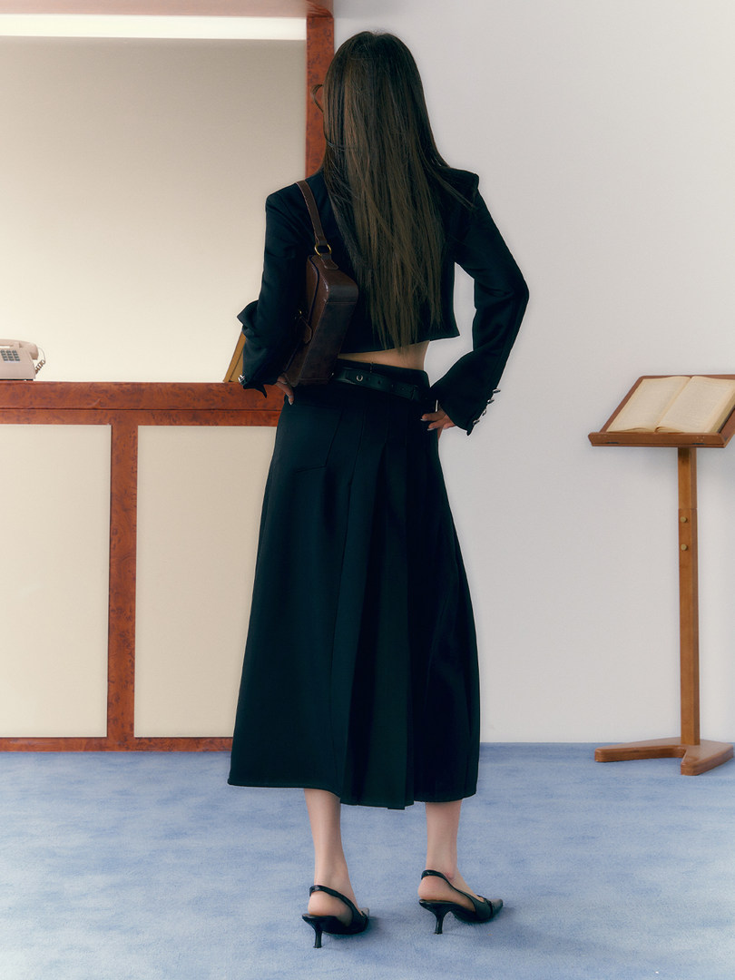 Model wearing a black cropped jacket and long skirt with heels and shoulder bag
