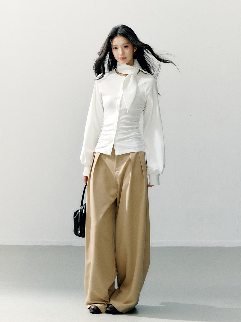 Model wearing a white blouse with a scarf tie and beige wide-leg trousers