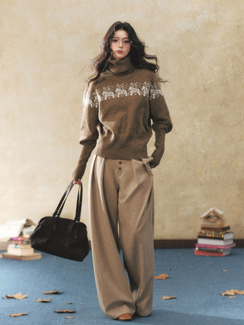 Model wearing a brown turtleneck sweater with wide-leg trousers and a black handbag