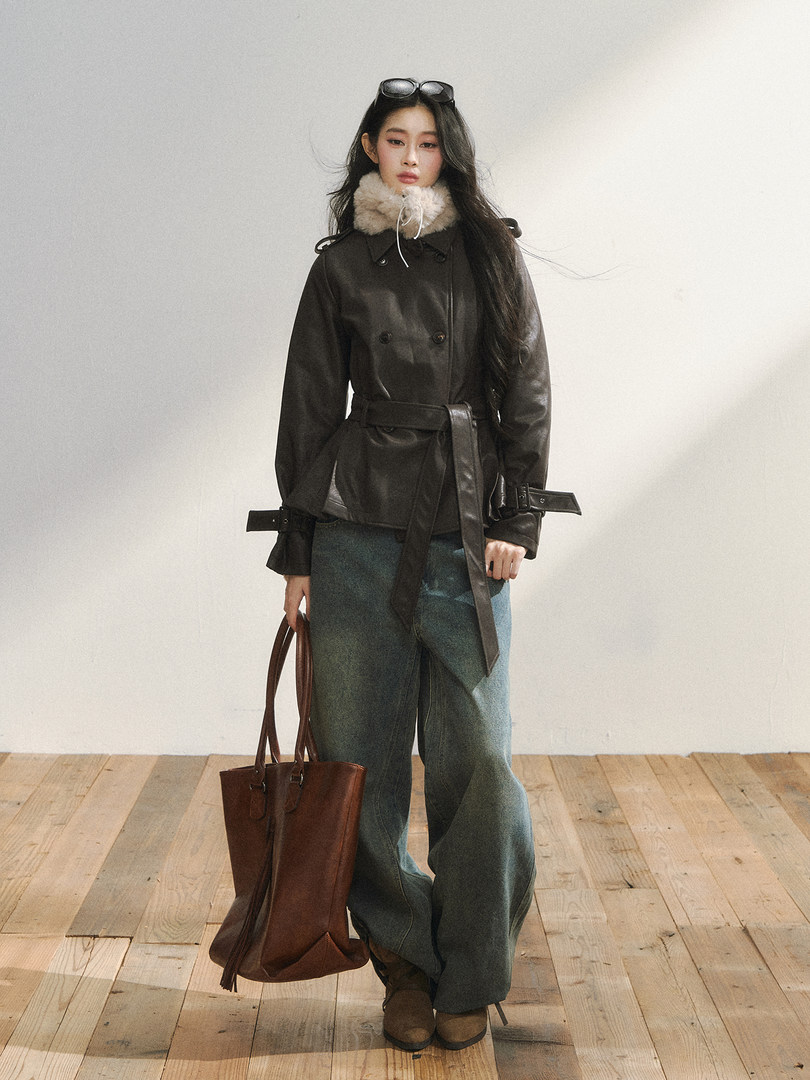 Model wearing a dark belted winter coat with fur collar, wide-leg pants, and a brown tote bag