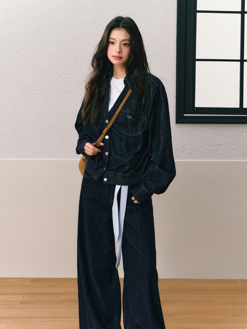 Model wearing a dark denim jacket and wide-leg jeans with a crossbody bag