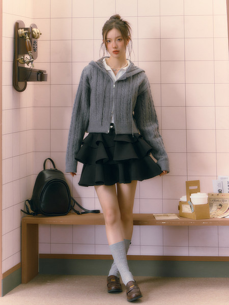 Fashion model wearing a gray cable-knit hoodie with a black ruffled skirt and socks
