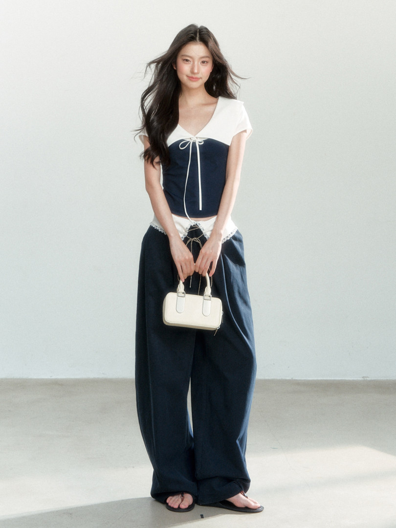 Model wearing a navy and white two-piece outfit with wide-leg pants and a small handbag