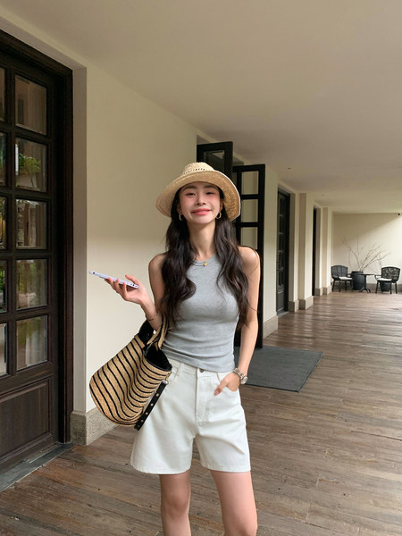 Woman wearing a gray sleeveless top with white shorts, a straw hat, and a woven tote bag