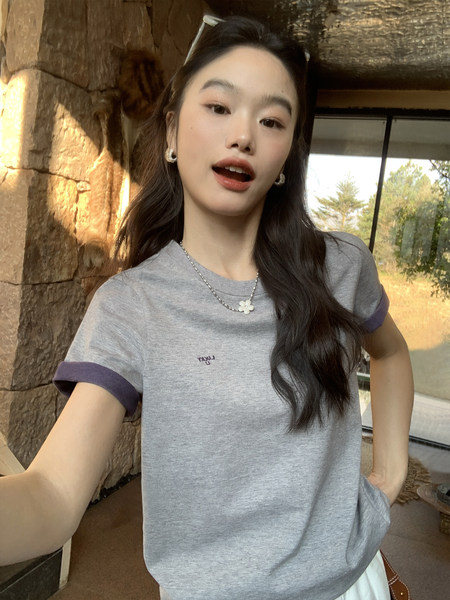 Woman wearing a gray short-sleeve T-shirt with purple trim and a small pendant necklace