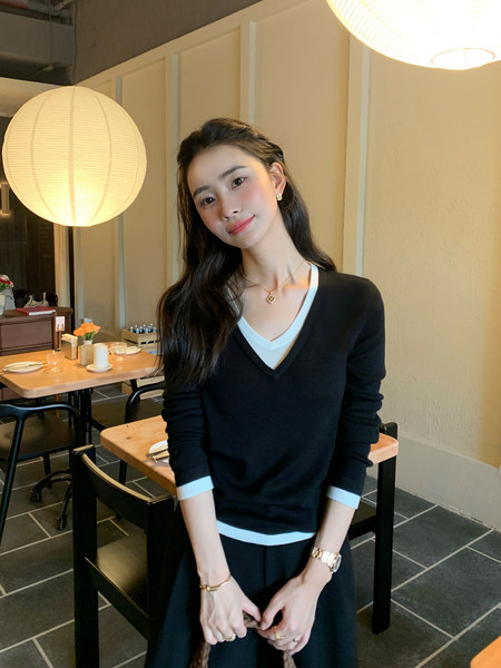 Woman wearing a black long-sleeve V-neck sweater with white trim in a cafe setting