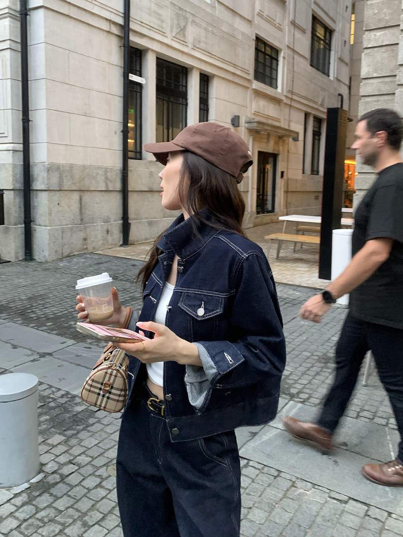 Woman wearing a dark denim jacket and jeans with a brown cap and plaid handbag