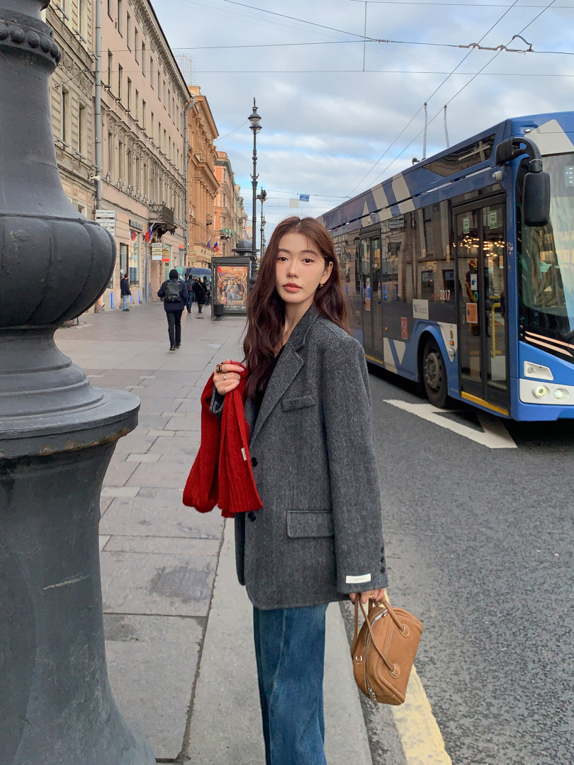 Woman wearing a gray blazer with jeans, a red scarf, and a tan handbag on a city street