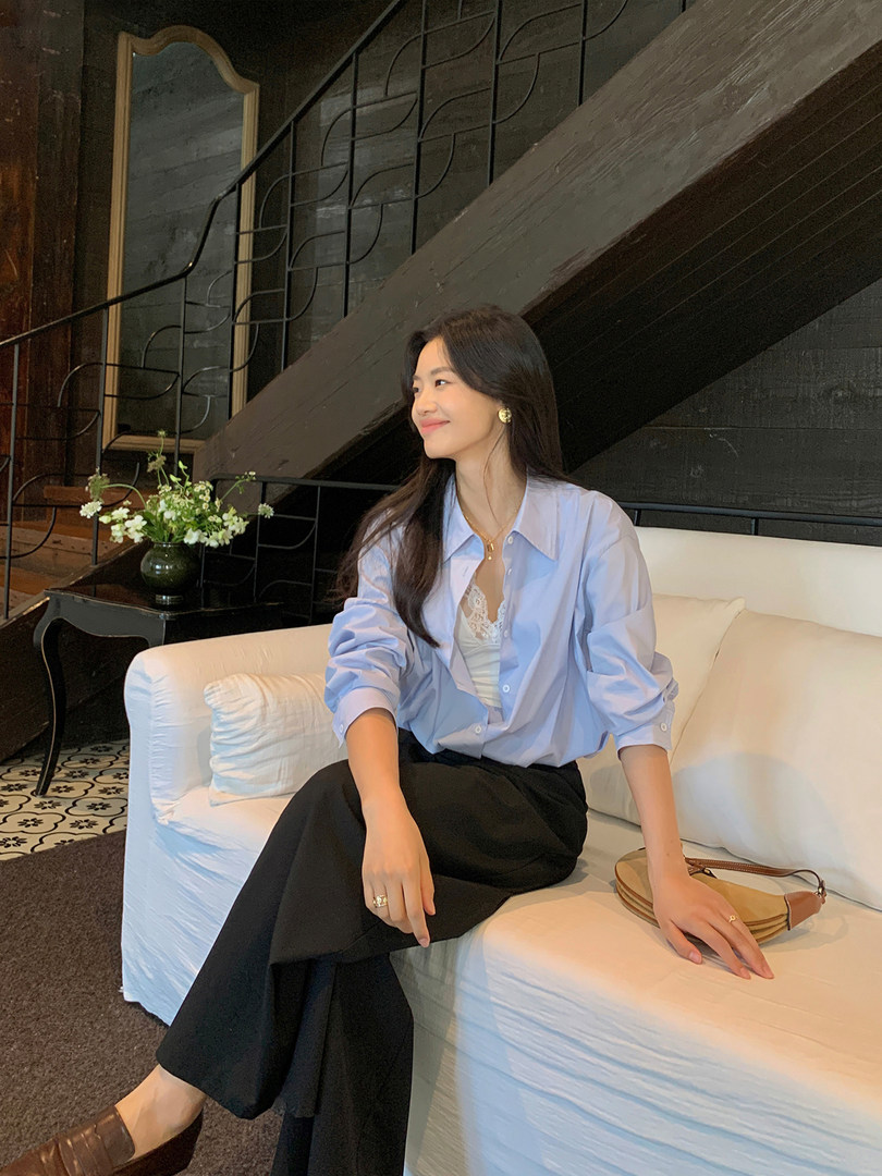 Woman wearing a light blue button-up shirt with black wide-leg pants on a sofa