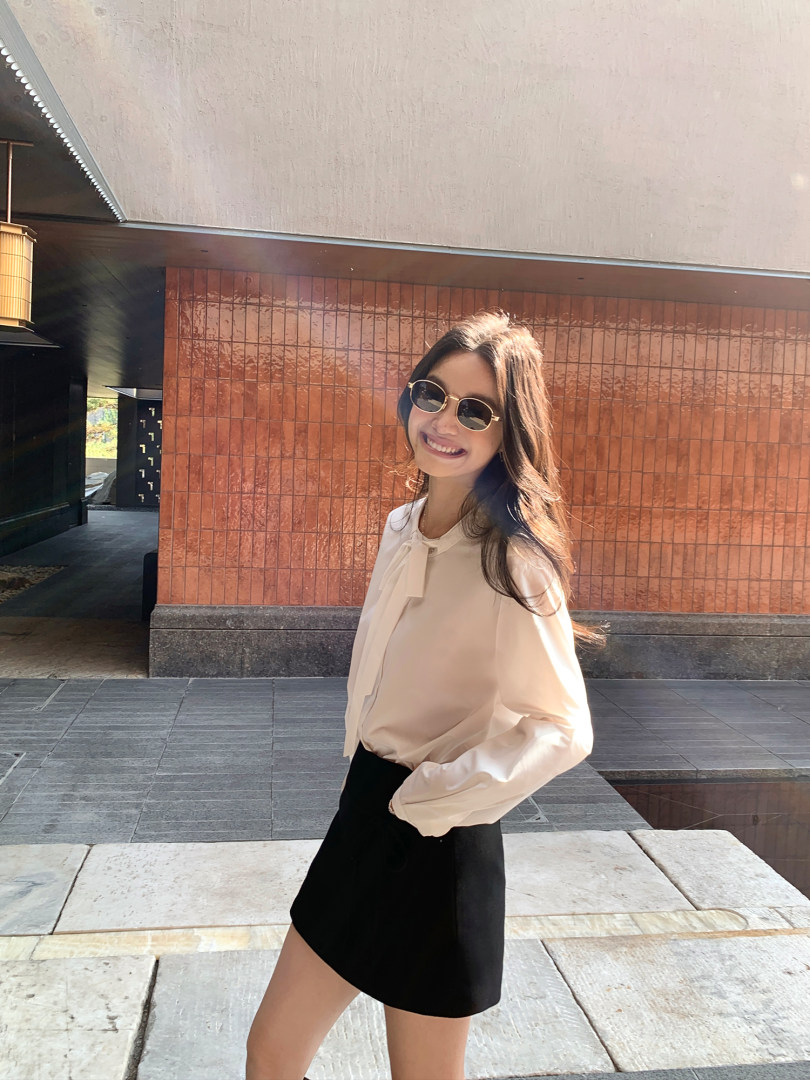 Woman wearing a cream blouse and black skirt outdoors