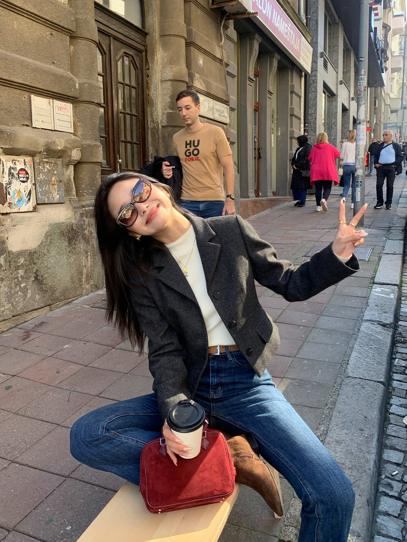 Woman wearing a dark blazer with jeans and a red bag sitting on a city street