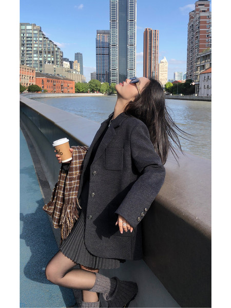 Woman wearing a dark wool coat and pleated skirt outdoors by a city waterfront