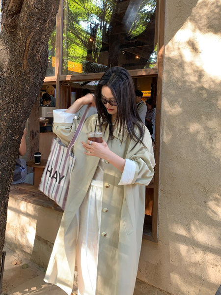 Woman wearing a cream oversized jacket and skirt set with a striped tote bag outdoors