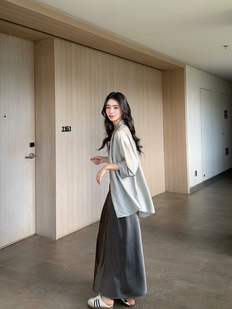 Woman wearing a light gray top and dark long skirt with white sneakers