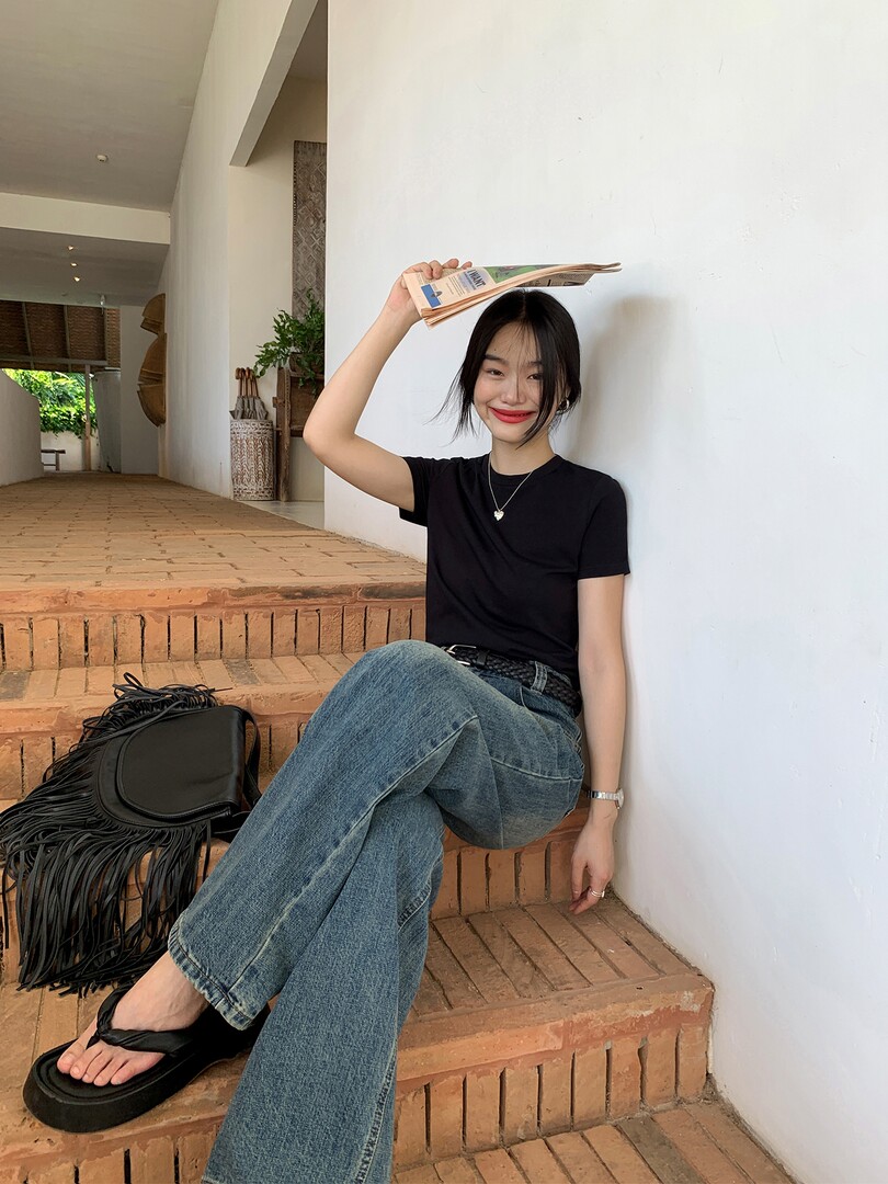 Woman wearing a black fitted T-shirt, blue wide-leg jeans, and black sandals while seated on brick steps