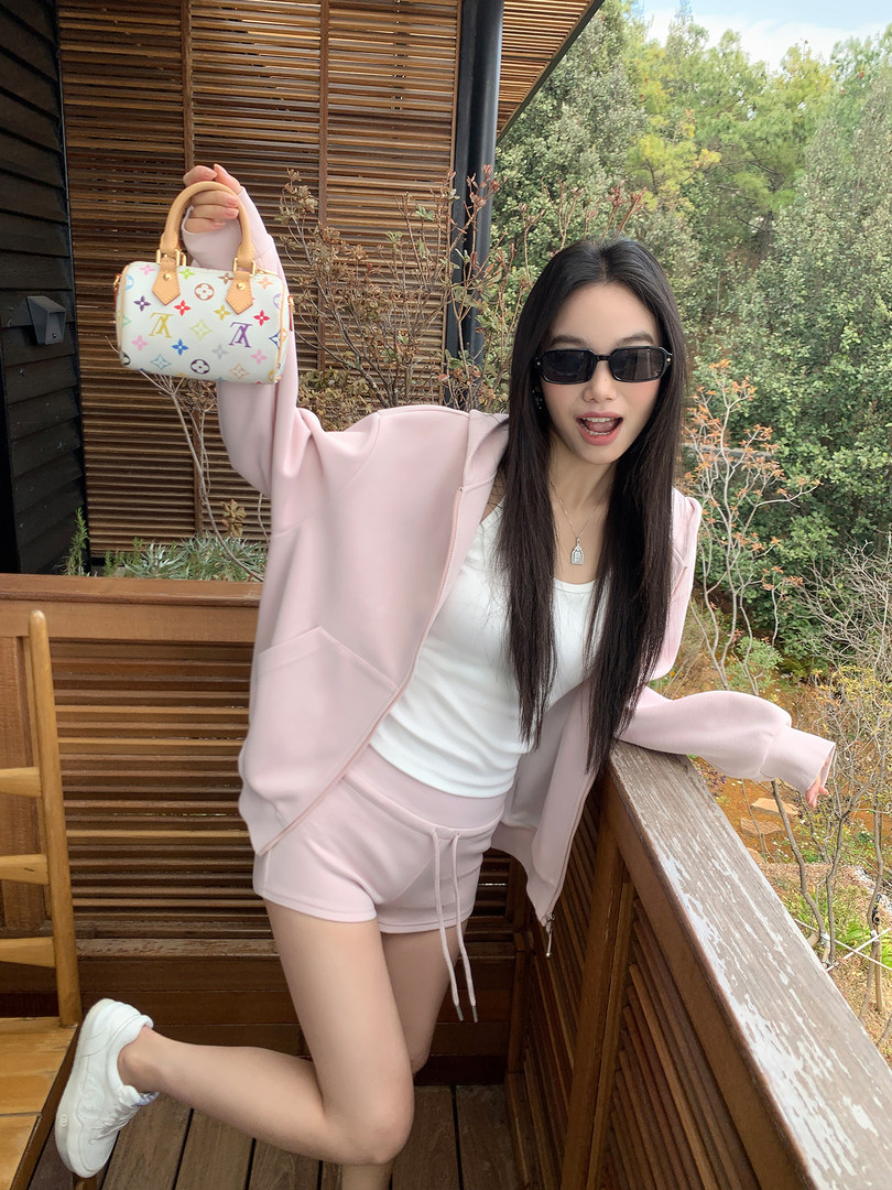 Woman wearing a light pink hoodie and shorts set while holding a small monogram handbag
