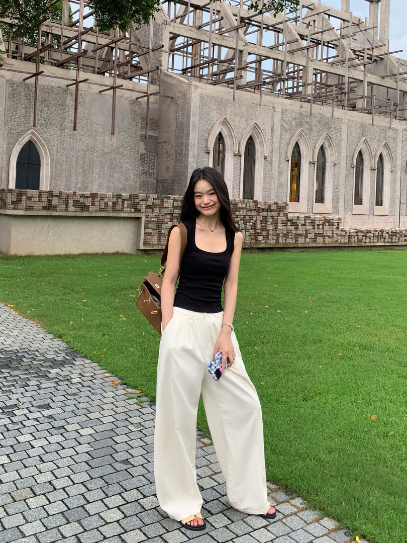 Woman wearing a black tank top with cream wide-leg pants outdoors