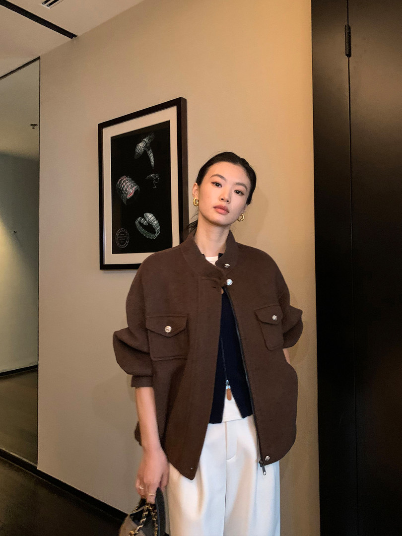 Woman wearing a brown zip-up jacket with flap pockets and white pants