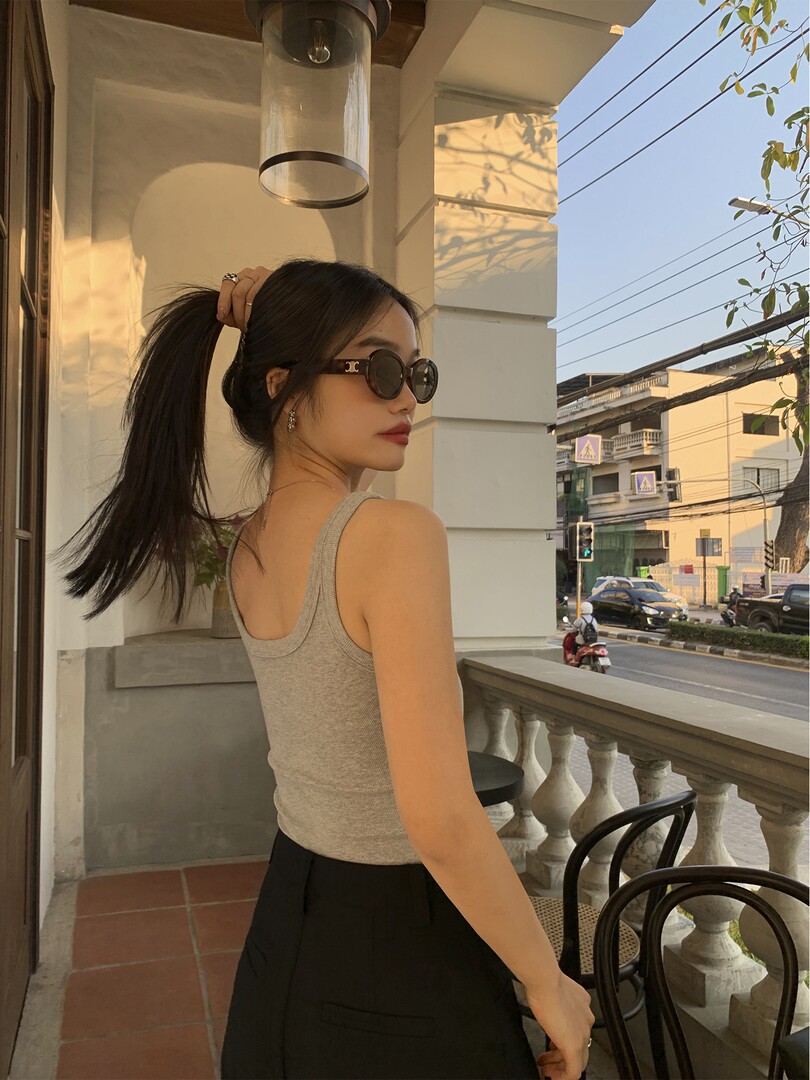 Woman wearing a gray ribbed tank top and black pants with round sunglasses outdoors