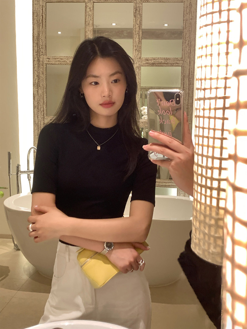 Woman wearing a black fitted short-sleeve top and white pants in a mirror selfie
