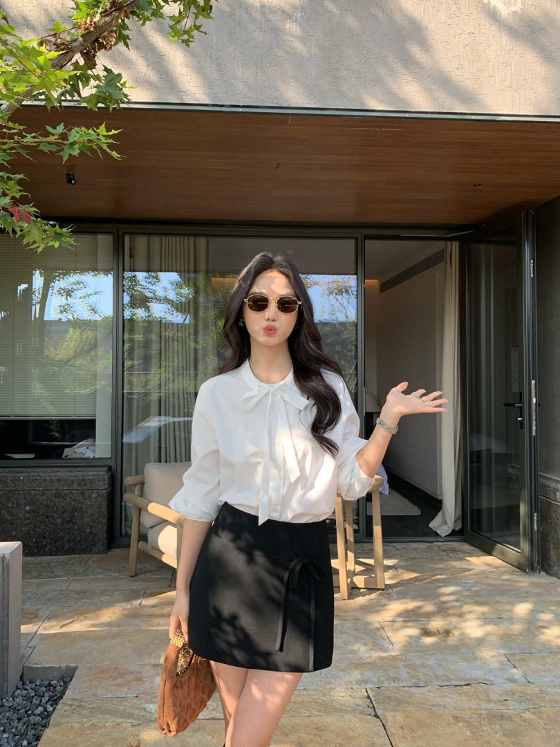 Woman wearing a white bow-tie blouse and black skirt outdoors