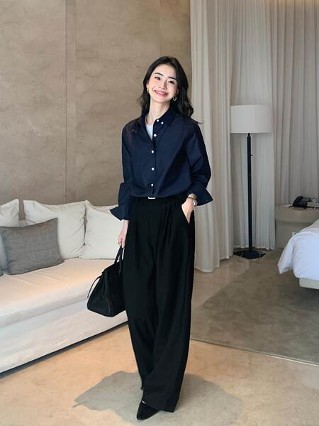 Woman wearing a navy button-up shirt with black wide-leg trousers and a black handbag