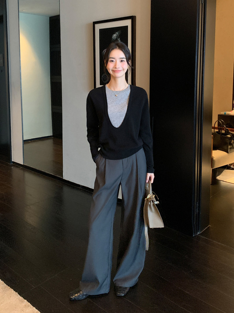 Woman wearing a black deep-V sweater with gray wide-leg trousers and a beige handbag