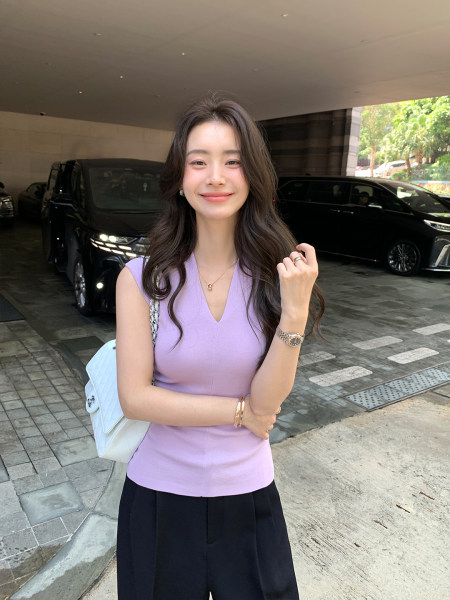 Woman wearing a light purple sleeveless V-neck top with a white handbag