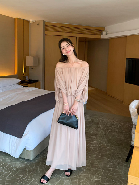 Woman wearing a beige off-shoulder maxi dress and holding a black clutch