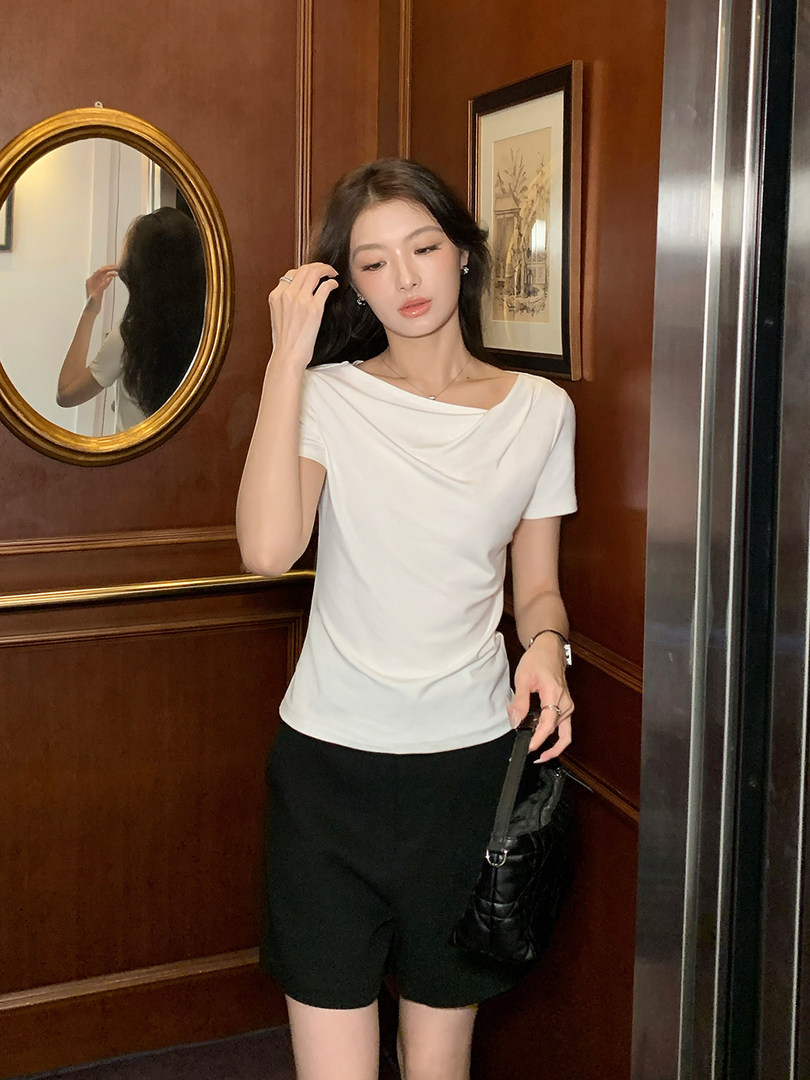 Woman wearing a white draped short-sleeve top with black shorts and a black handbag