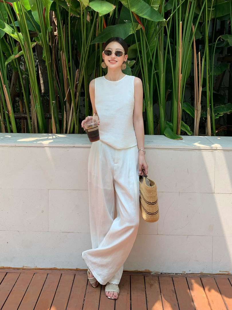 Woman wearing a white sleeveless top and wide-leg pants with a straw bag outdoors