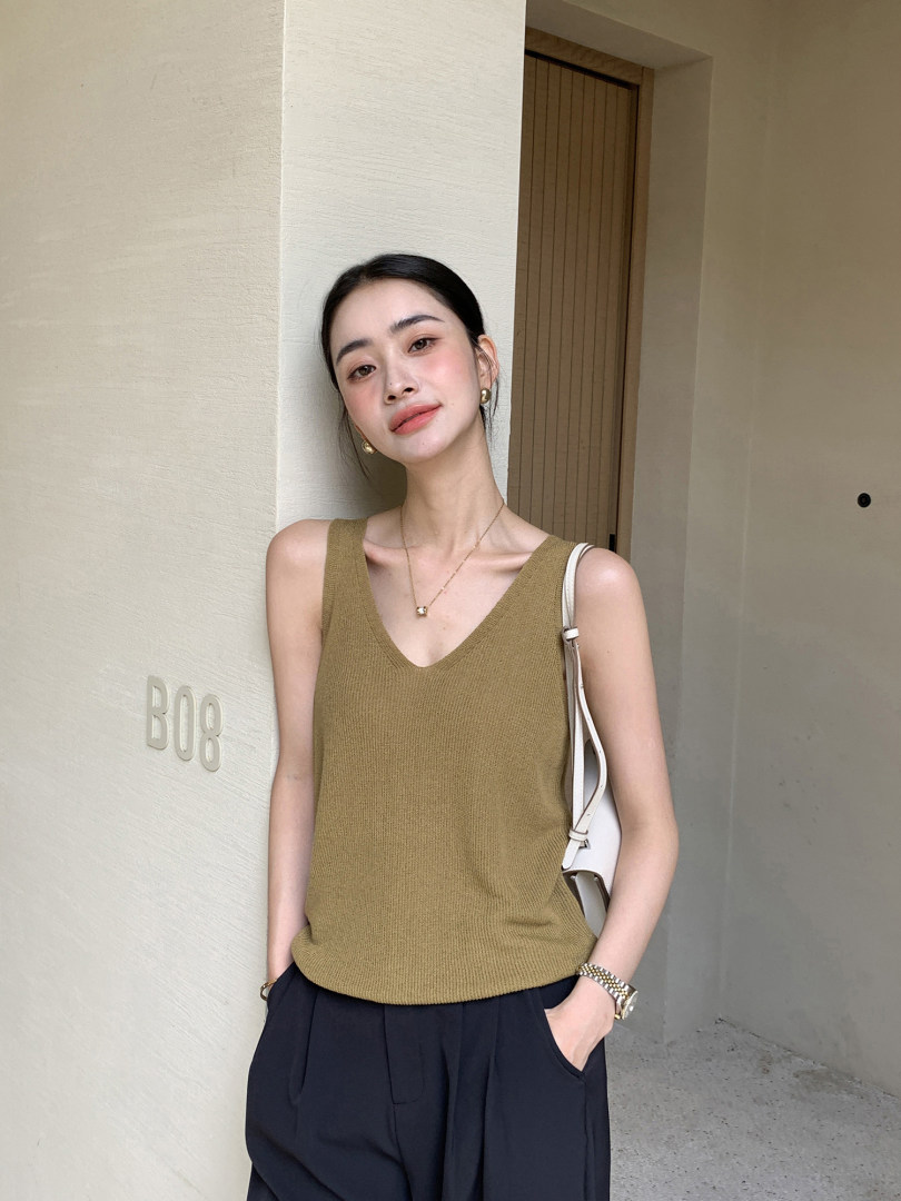 Woman wearing an olive sleeveless knit tank top with navy pants and a white shoulder bag