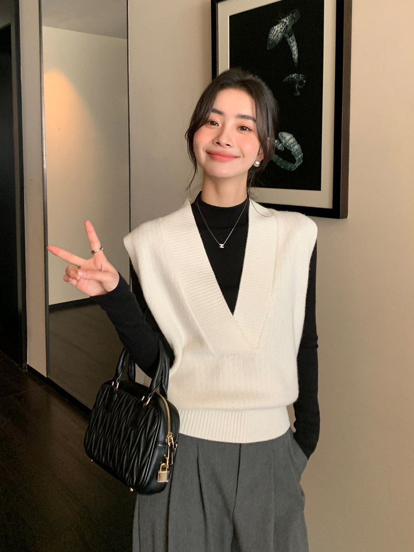 Woman wearing a white knit sweater vest over a black top with a black handbag