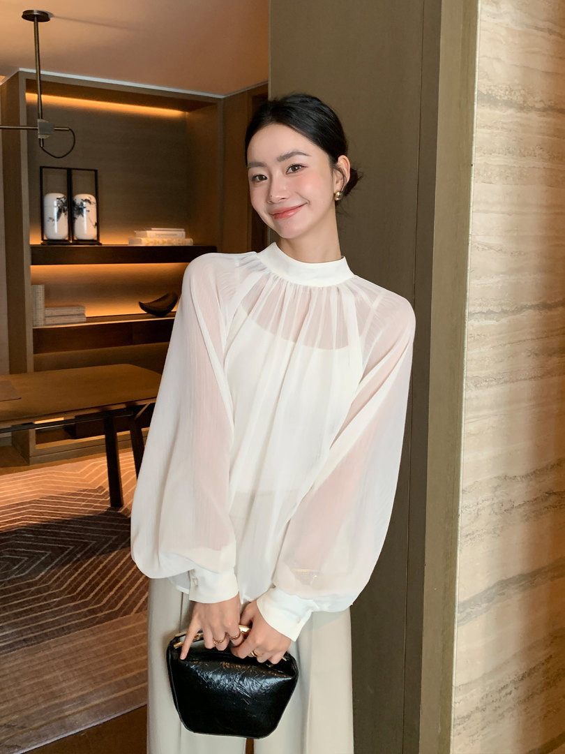 Woman wearing a sheer white blouse and holding a black handbag
