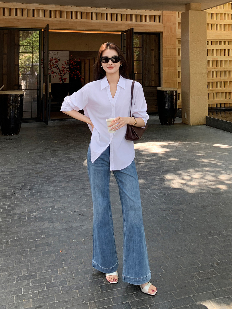 Woman wearing a white button-up shirt and flared blue jeans with sandals