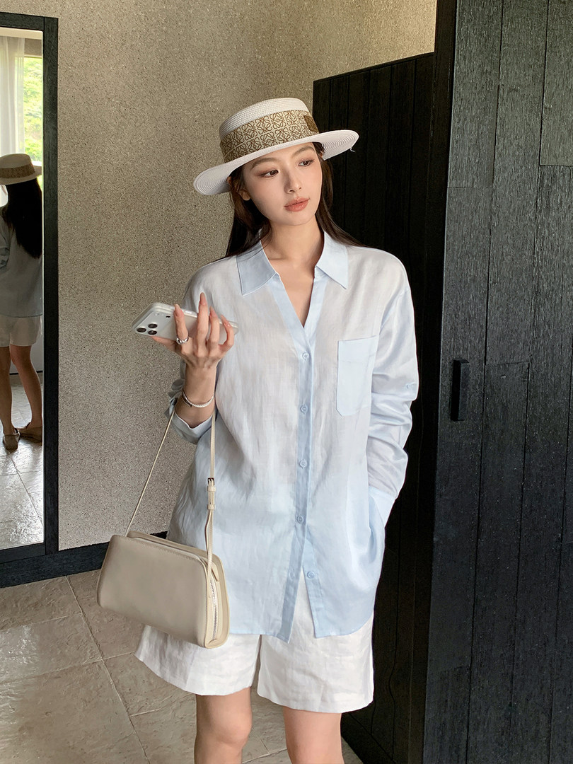Model wearing a light blue button-up shirt with white shorts, a hat, and a shoulder bag