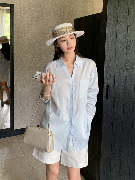 Model wearing a light blue button-up shirt with white shorts, a hat, and a shoulder bag