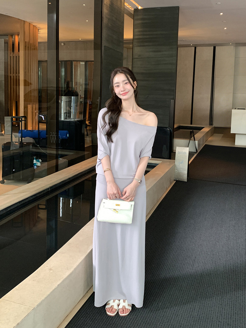 Woman wearing a light gray off-shoulder maxi dress and holding a white handbag