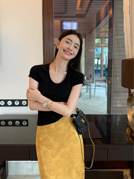 Woman wearing a black fitted top with a yellow patterned skirt and black quilted handbag