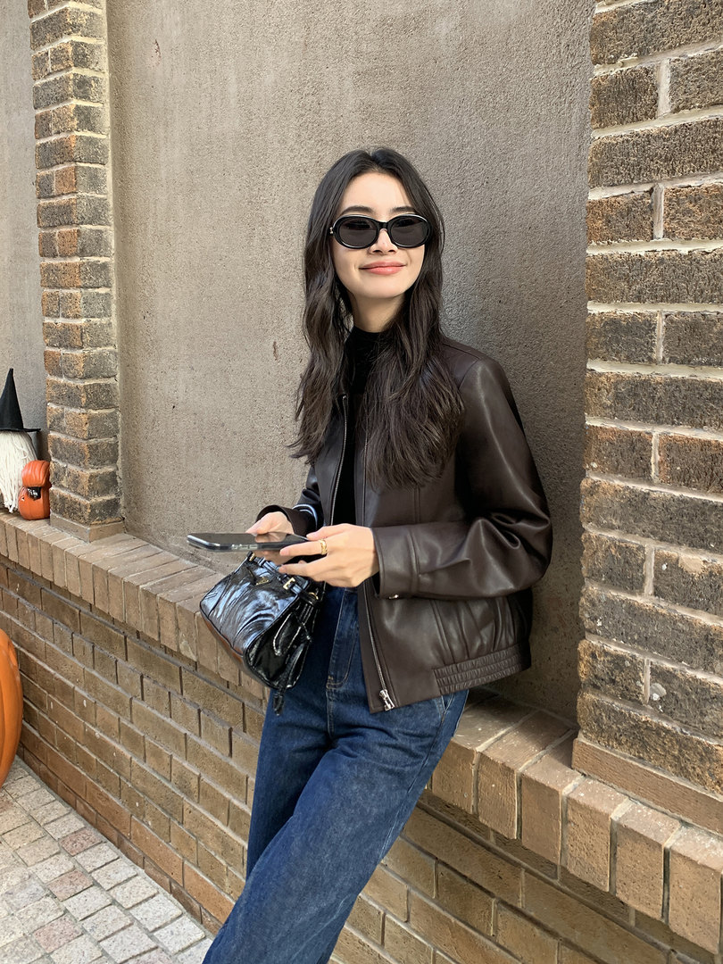 Woman wearing a dark brown leather jacket with sunglasses and a black handbag