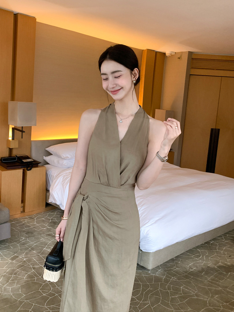 Woman wearing a sleeveless olive wrap dress in a hotel room